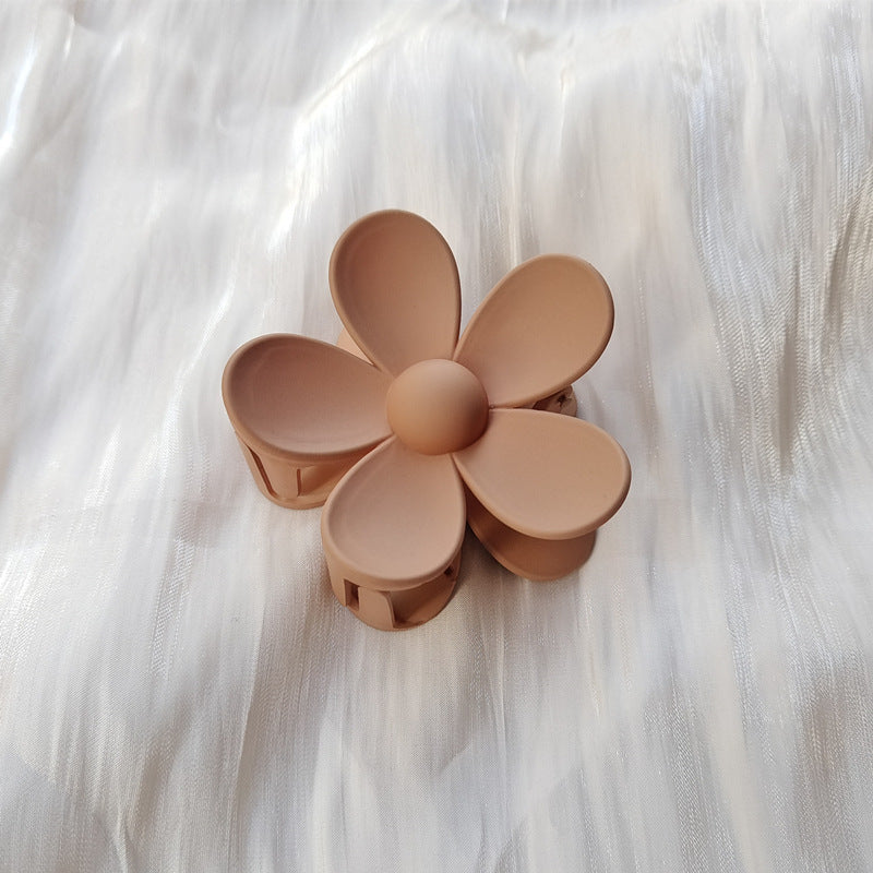 Colorful flower hair clip in matte pastel brown with five rounded petals on white fabric background