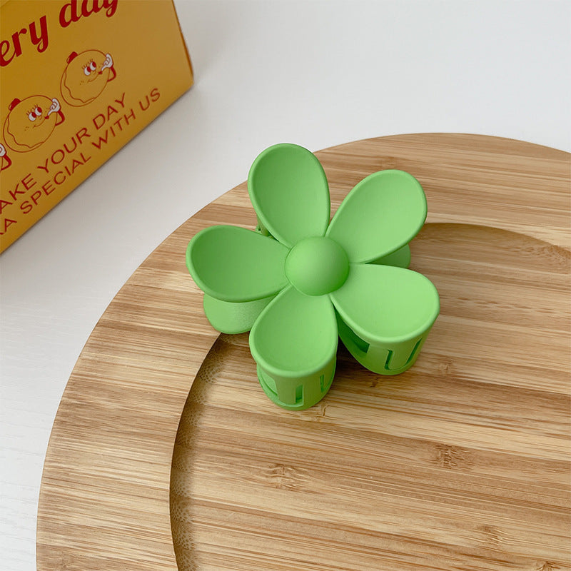 Green colorful flower hair clip with frosted finish placed on a wooden surface
