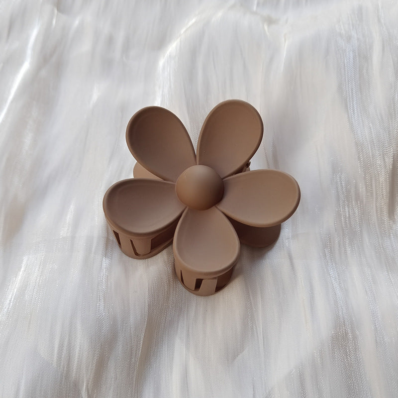 Matte brown colorful flower hair clip with five petals on white textured fabric background