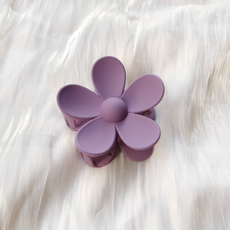 Purple colorful flower hair clip with frosted matte finish on white fabric background