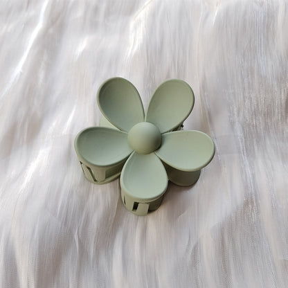 Green frosted colorful flower hair clip with five rounded petals on a light fabric background