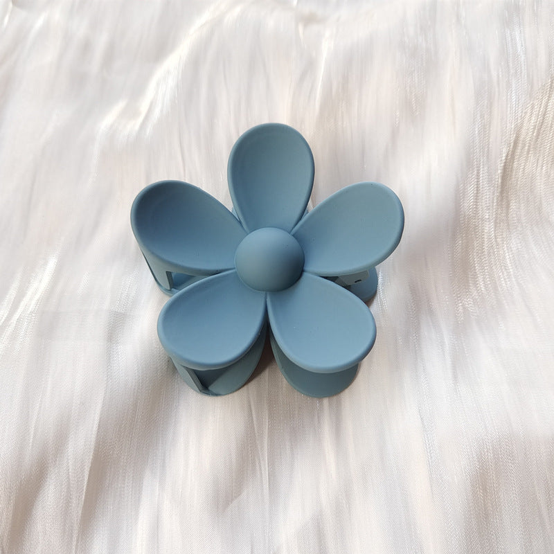 Blue colorful flower hair clip with frosted finish placed on white fabric background