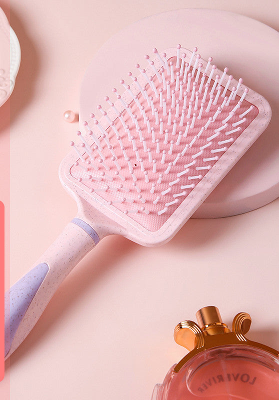Pink professional airbag comb with cushioned bristles and ergonomic handle on a soft pink background